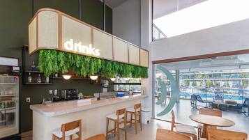 Zona de bar moderna con un letrero que dice 'drinks', taburetes de madera y vista a la piscina.