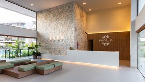 A modern reception area with a stone wall, a wooden reception desk, and a seating area with cushions. - Malia Beach #a301 - Resort por Carpediem (Ipojuca)