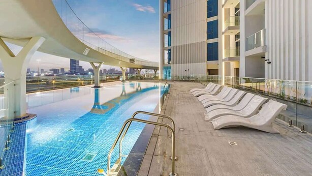 En pool på taket med modern design, omgiven av solstolar och ett glasräcke.
