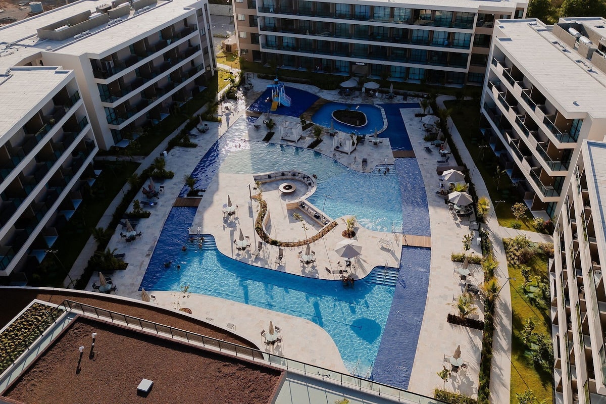 Un hotel moderno con una piscina central, varios balcones y una zona ajardinada alrededor de la piscina.