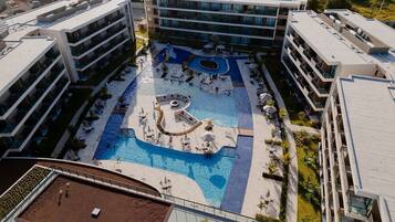 Um hotel moderno com piscina central, várias varandas e área de piscina ajardinada.