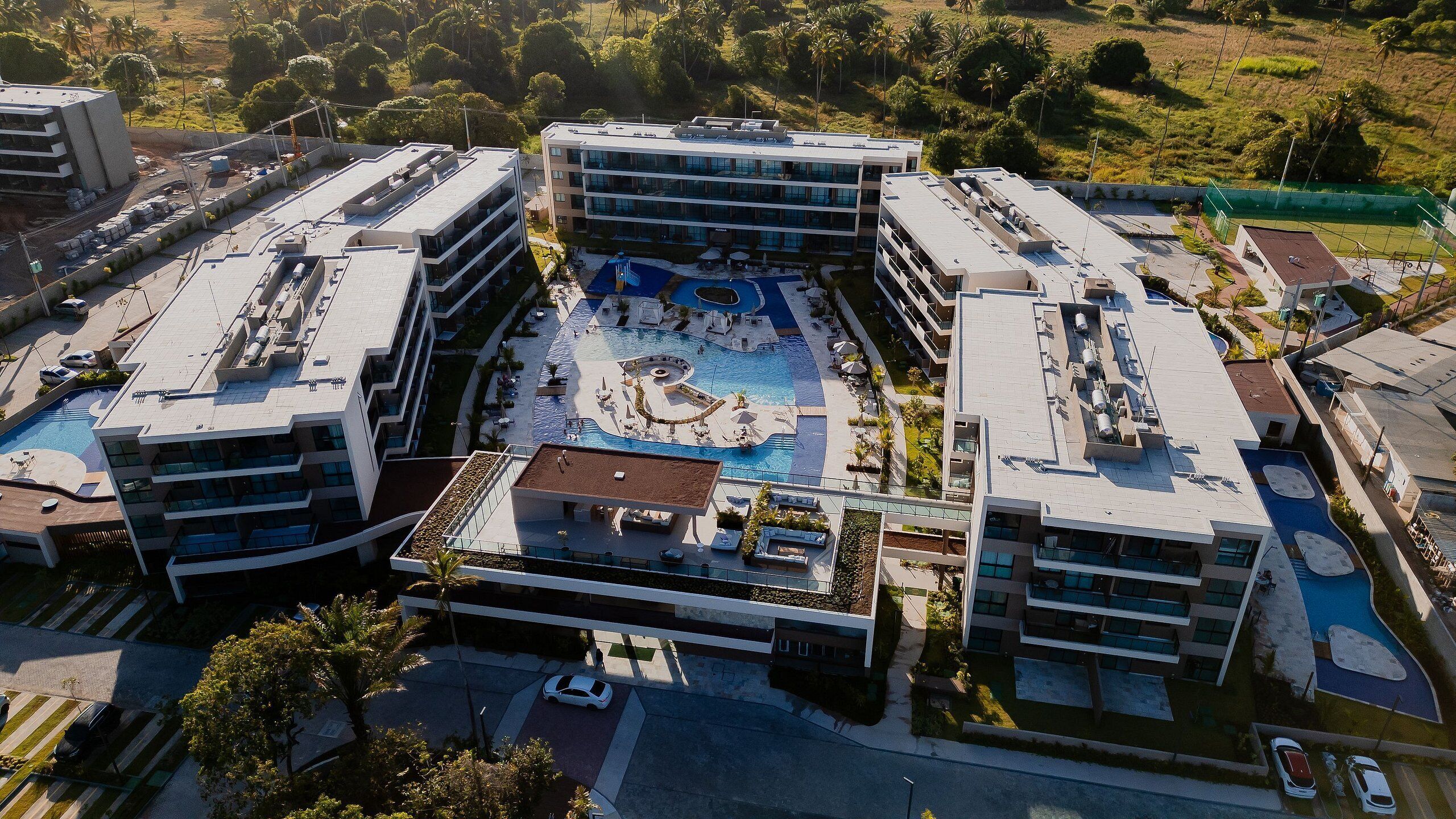 Un moderno complejo hotelero con varias edificaciones, una piscina central y zonas verdes circundantes.
