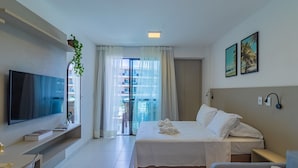 Habitación de hotel con cama, televisión, escritorio, silla, balcón y vistas a edificios, además de una planta.
