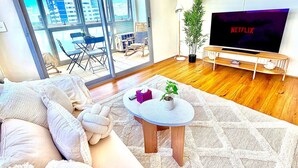 Un salon moderne avec une grande fenêtre, un téléviseur à écran plat, un canapé, une table basse et une petite plante.
