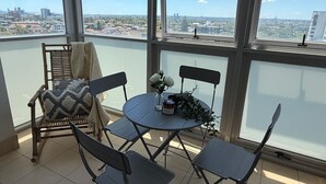 Un balcon donnant sur le paysage urbain, une table ronde avec des chaises et un fauteuil en osier avec une couverture.