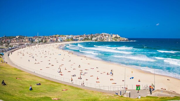 Une plage avec une promenade dallée, une zone herbeuse et un paysage urbain en arrière-plan.