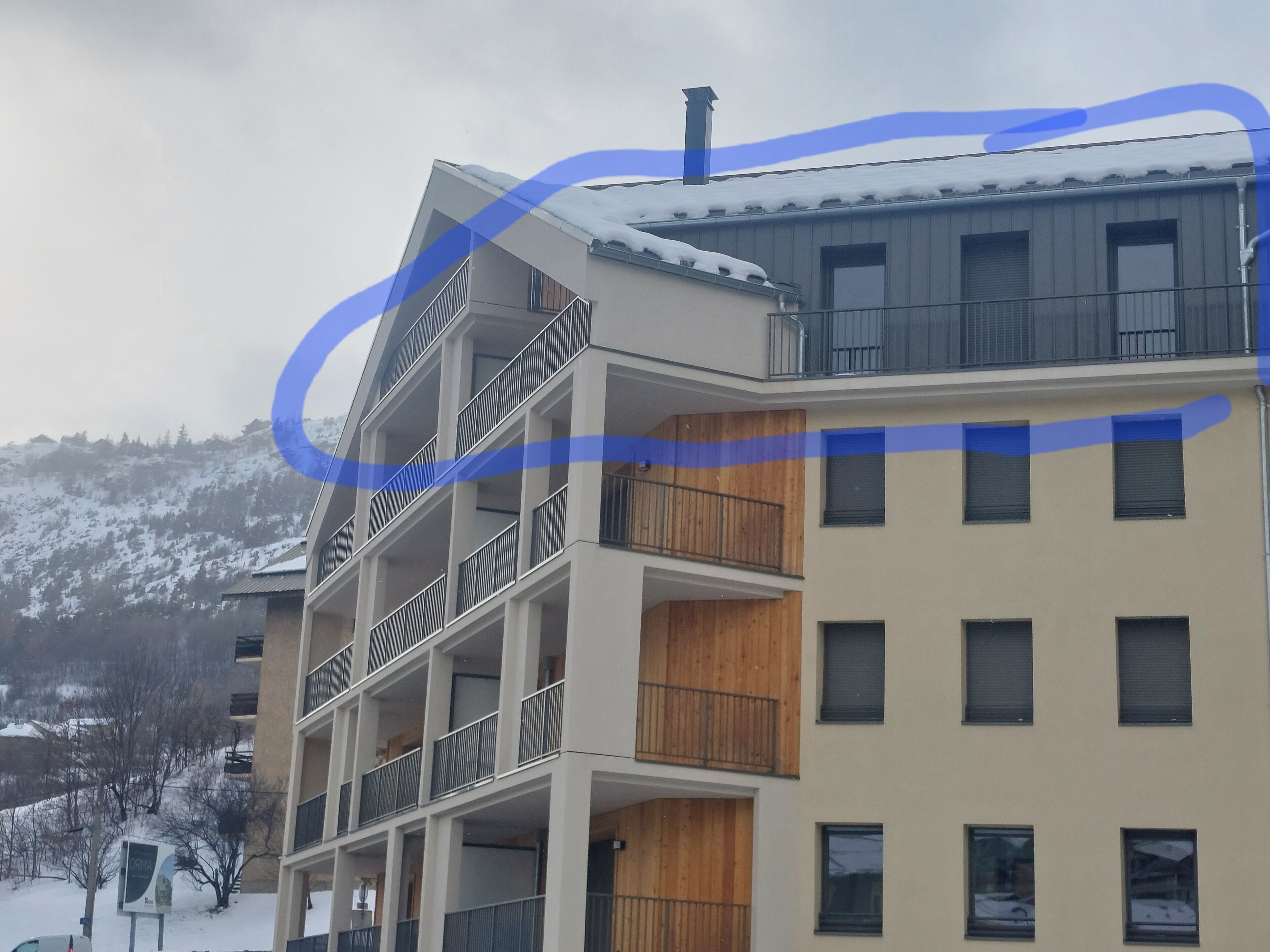 A multi-story building with balconies, a chimney, and a snowy landscape in the background.