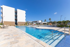 A swimming pool area with lounge chairs and a building with balconies. - Makia Beach #d307 - Flat With Balcony by Carpediem (Ipojuca)