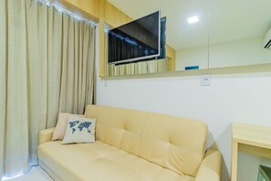 A beige sofa with a world map pillow, a mounted flat-screen TV, and a wooden side table in a room with light-colored walls and curtains. - Makia Beach #d307 - Flat With Balcony by Carpediem (Ipojuca)