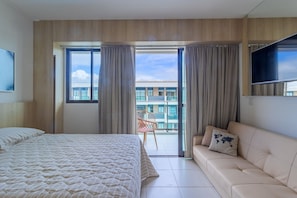 A hotel room with a bed, a sofa, a TV, and a balcony with a chair. - Makia Beach #d307 - Flat With Balcony by Carpediem (Ipojuca)