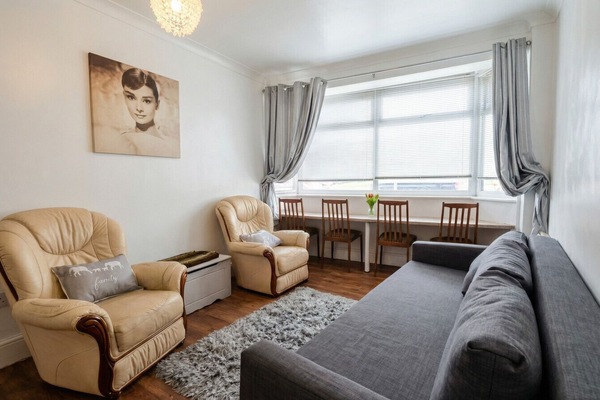 Living room with two leather armchairs, grey corner sofa, wall art, a large bay window with grey curtains, and a dining table with chairs positioned by the window.