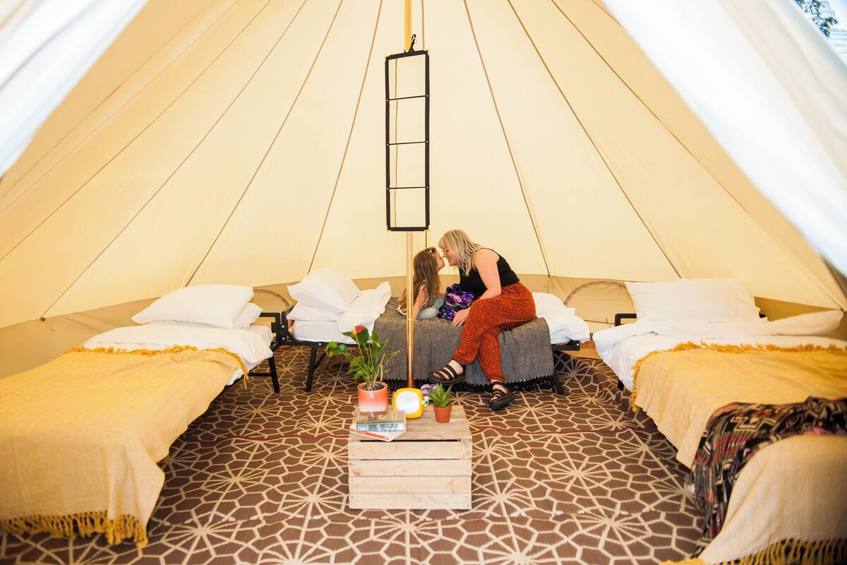 A cozy tent with two beds, a central table with books and plants, and a hanging ladder.