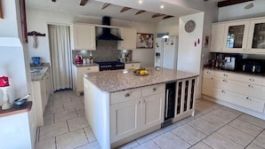 A kitchen with a central island, white cabinets, a black range hood, and a tiled floor. - Dordogne Maison & Gîte with Pool, Gardens and Terraces Near Bergerac (Pomport)