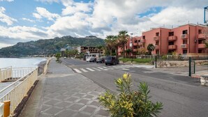 Eine Küstenstraße mit Fußgängerweg, parkenden Autos und einem Gebäude mit Balkonen.