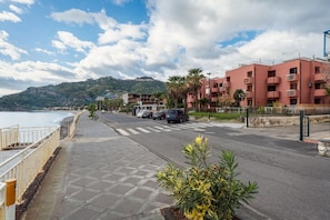 Una strada costiera con marciapiede, auto parcheggiate e un edificio con balconi.