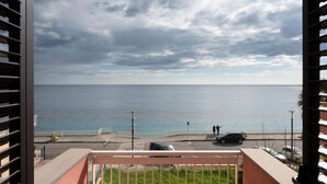 Ein Balkon mit Meerblick, eine Straße mit Autos und eine Fußgängerampel.