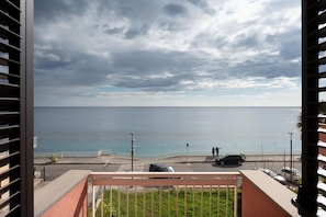 Un balcone con vista sul mare, una strada con auto e un attraversamento pedonale.