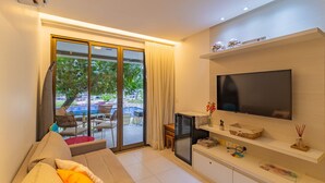 A modern living room with a sofa, a TV, and a sliding glass door leading to an outdoor area with a pool. - Malawi #104a - Seaside Apartment by Carpediem (Ipojuca)