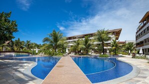 A resort pool area with two large pools, a central walkway, and a multi-story building in the background. - Malawi #104a - Seaside Apartment by Carpediem (Ipojuca)