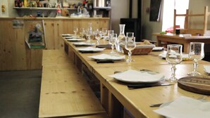 A long wooden table set for dining with multiple wine glasses and plates, a basket, and a wooden board with a logo. - Gite du Souillet à la Ferme (Noyarey)