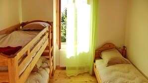 A room with two wooden bunk beds, a window with a green curtain, and a wooden floor. - Gite du Souillet à la Ferme (Noyarey)