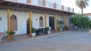 Un edificio con un patio techado, mobiliario exterior y una palmera.