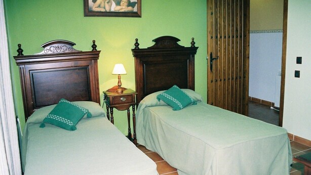Una habitación con dos camas, una mesita de noche con lámpara, una puerta de madera y una pared verde.