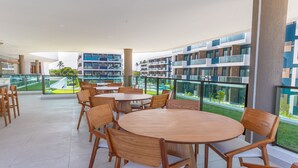 Un espacio moderno para comer al aire libre con mesas y sillas de madera redondas, con vistas a una piscina y un jardín ajardinado.