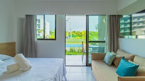 Habitación de hotel con cama, sofá y vistas a una piscina y follaje.