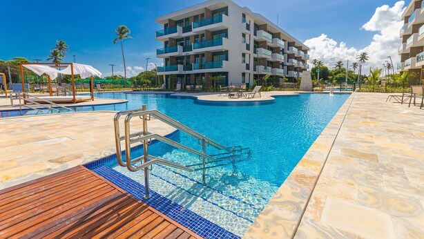Un hôtel moderne doté d’une piscine, de nombreux balcons et offrant une vue sur un ciel d’un bleu éclatant.