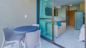 Una cocina moderna con refrigerador, un comedor con mesa y sillas, y un vidrio corredizo que da a una sala de estar con sofá y mesa de centro.
