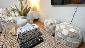 A living room with a television mounted on the wall, a lamp, a vase with plants, a remote control, and a tissue box on a woven table.