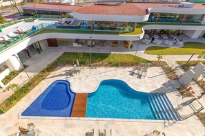Un hotel moderno con una amplia piscina exterior, varias zonas de comedor y una terraza en la azotea.
