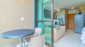 Et moderne køkken med et køleskab, et spiseområde med et rundt bord og stole, samt en opholdsstue med en sofa og en glasdør, der fører ud til en balkon.