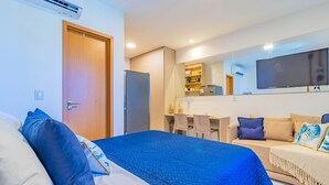 A hotel room with a bed, a sofa, a desk, a television, and a kitchenette. - Makia Beach #b308 - em Muro Alto por Carpediem (Ipojuca)