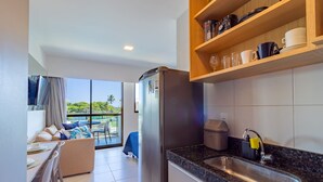 A modern kitchen with a stainless steel refrigerator, a granite countertop sink, and a dining area with a table and chairs. - Makia Beach #b308 - em Muro Alto por Carpediem (Ipojuca)