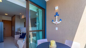 A modern living room with a sofa, a dining table with a candle, and a large window with curtains. - Makia Beach #b308 - em Muro Alto por Carpediem (Ipojuca)