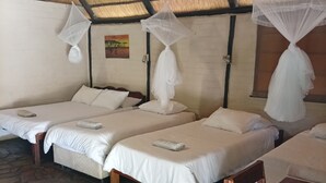 Ein Zimmer mit drei Betten, jedes mit weißer Bettwäsche und Moskitonetzen. Der Raum hat einen Steinfußboden und ein Strohdach.