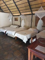 Ein Zimmer mit drei Betten, jedes mit weißer Bettwäsche und Moskitonetzen. Der Raum hat einen Steinfußboden und ein Strohdach.