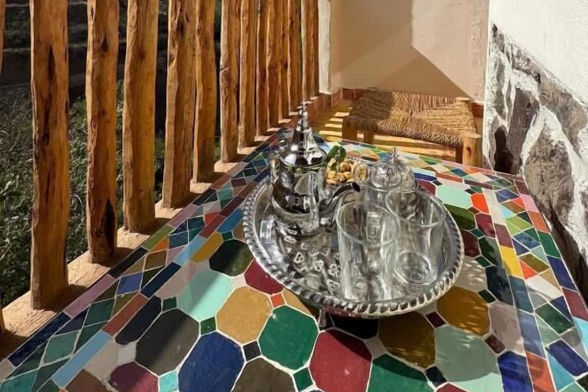 Un balcón con barandilla de madera, suelo de mosaico y una mesa con bandeja de vidrio y cubiertos.