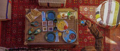 A dining table set with various dishes and utensils, surrounded by patterned rugs and a striped chair.