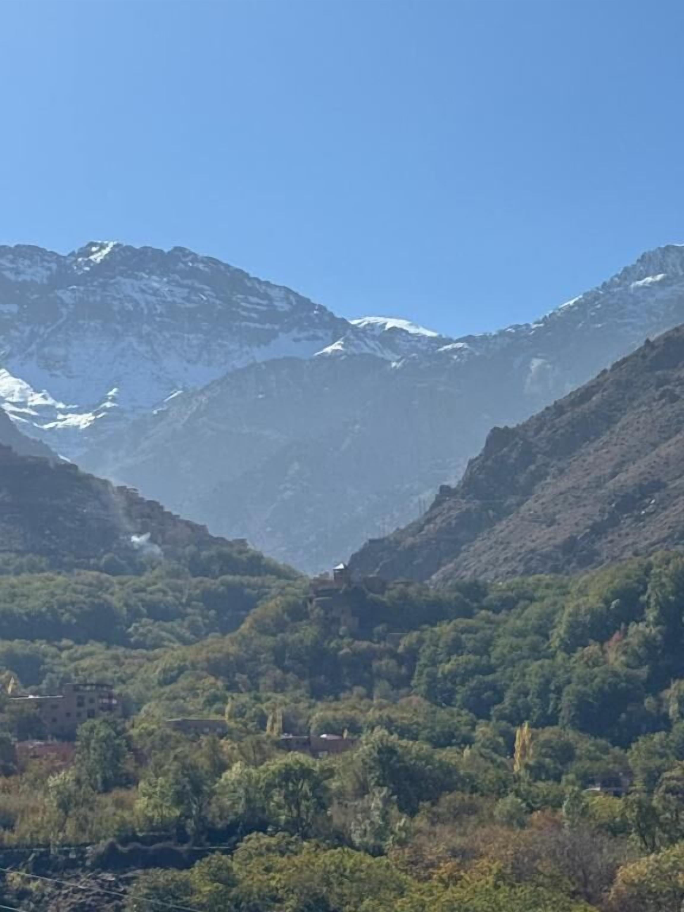 Un paysage montagneux avec une vallée et un petit bâtiment niché au milieu des arbres.