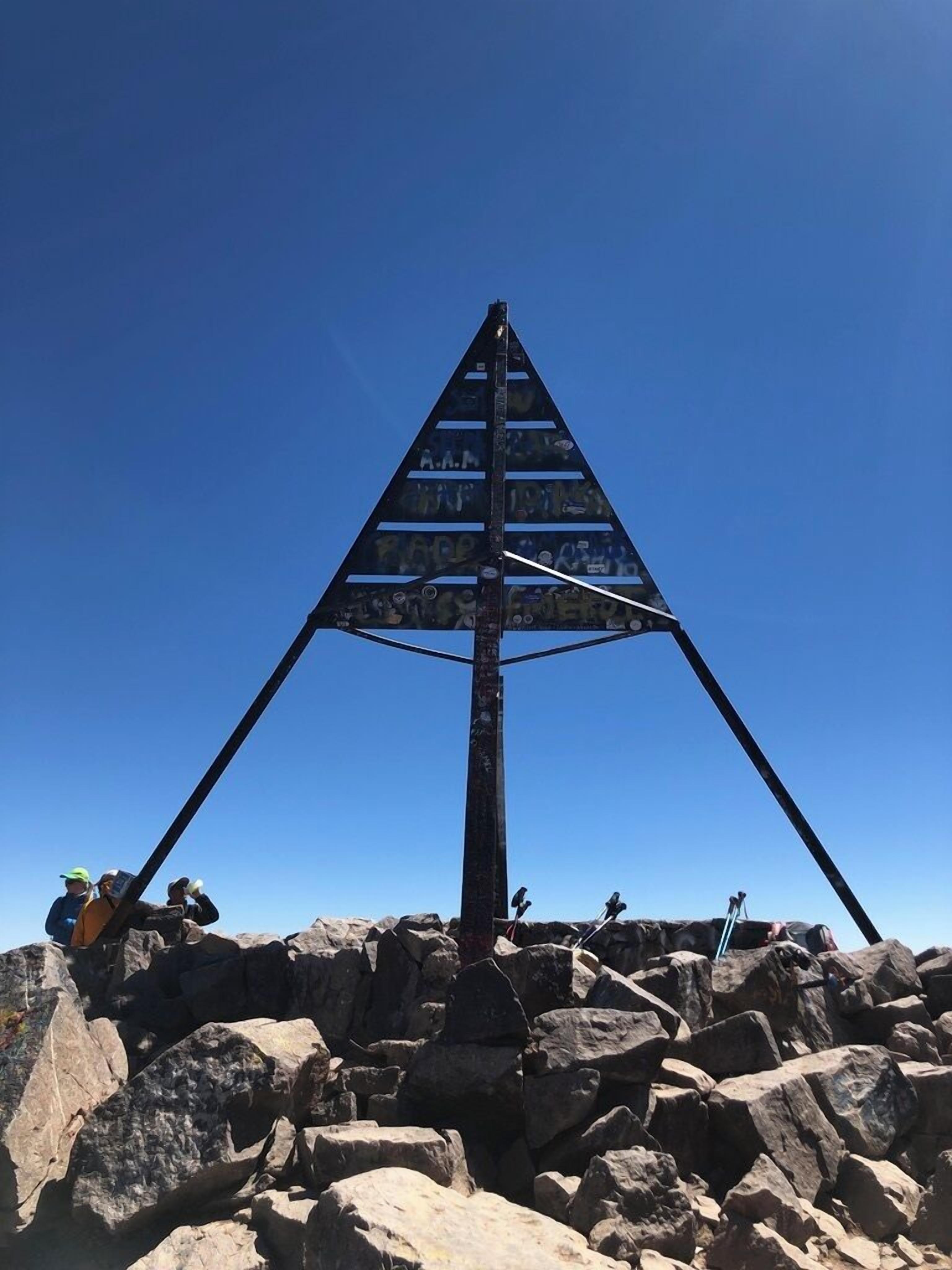 A large metal structure resembling a pyramid with graffiti on its surface, set on rocky terrain.