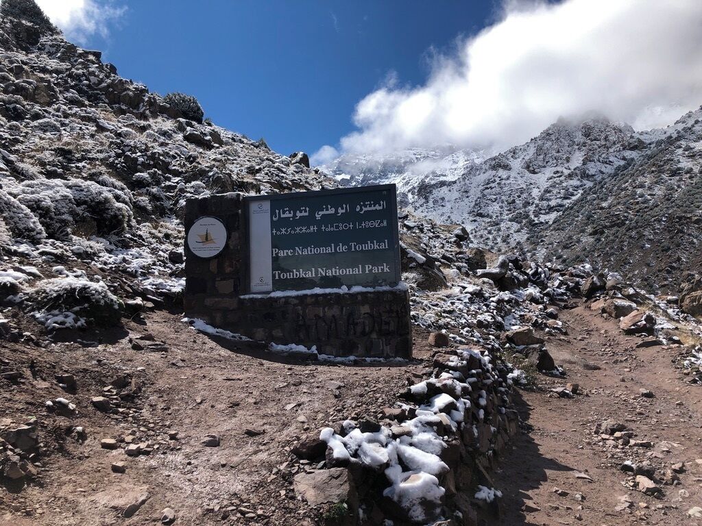 A sign for Parc National de Toubkal with a rocky path and snow patches.