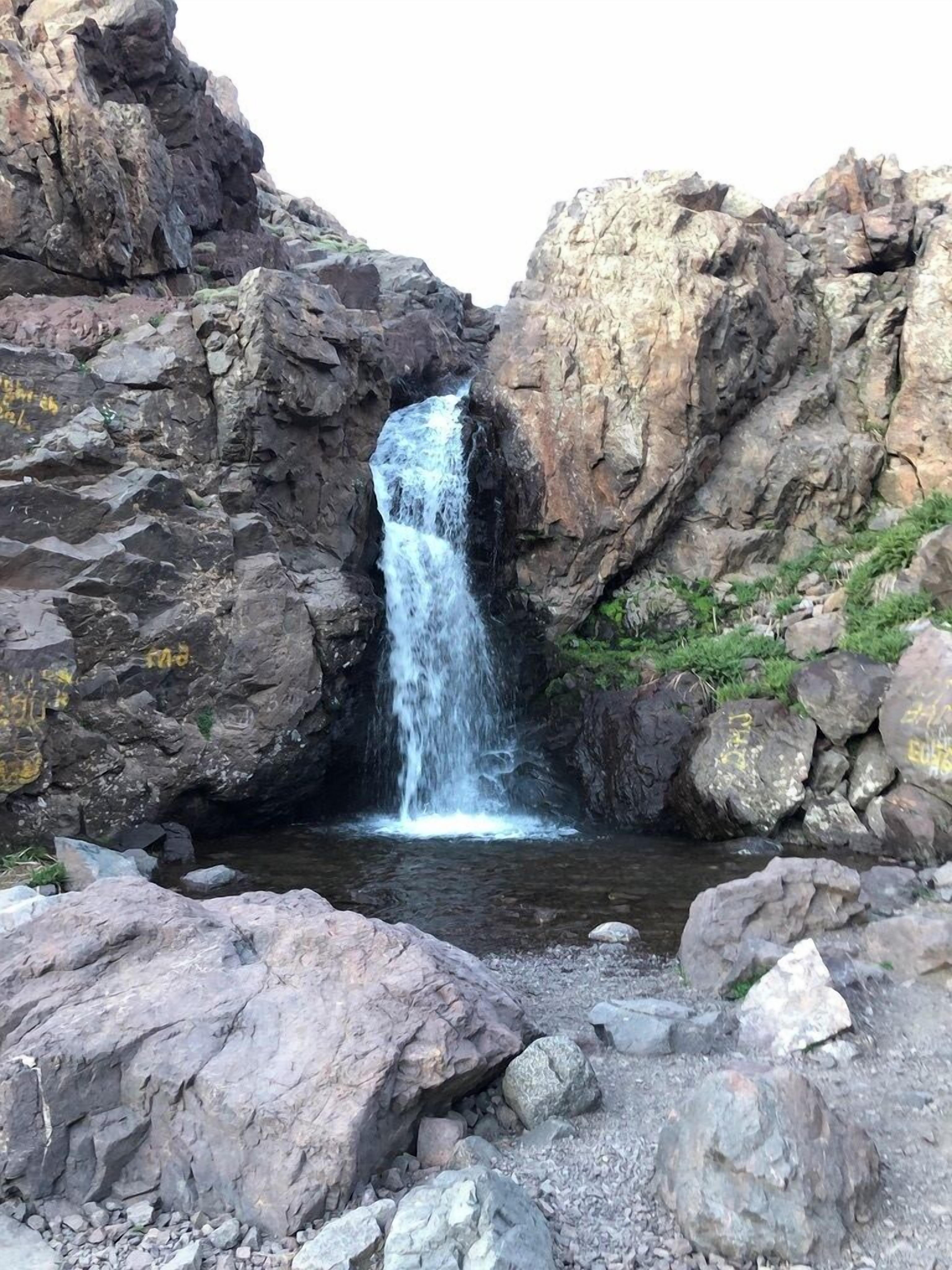 A waterfall cascading down a rocky cliff into a pool surrounded by large boulders.