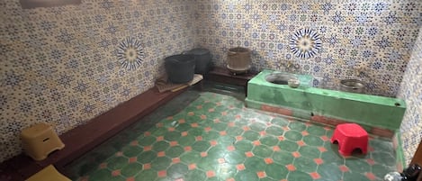 Een kamer met een vloer van groene en oranje tegels, een houten bankje, een rode kruk en een behang met patroon.