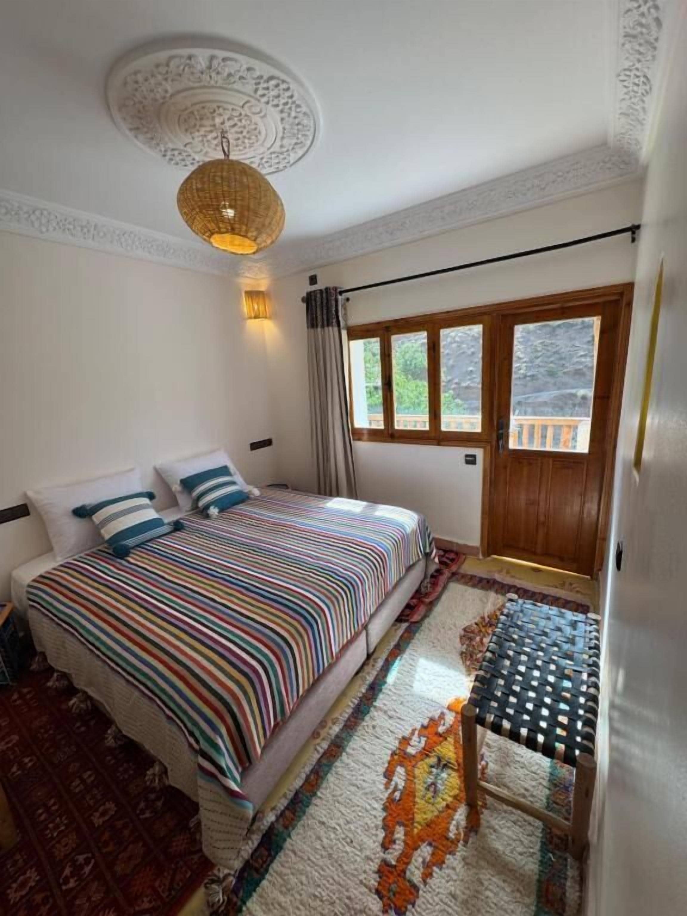 A bedroom with a bed, a window, a door, and a ceiling light fixture.