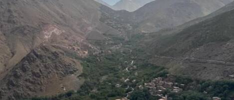 Un paisaje montañoso con un valle que alberga un pequeño asentamiento, casas y algunos coches aparcados a lo largo de la carretera.