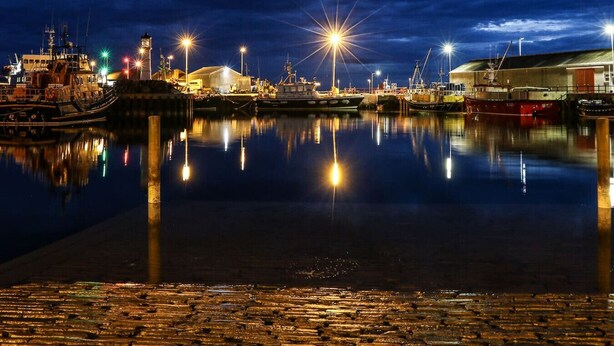 A nighttime harbor with boats docked, calm water reflecting lights, and a paved waterfront. - Havrock with harbour view near town centre (Orkney)