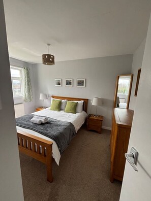 A bedroom with a wooden bed, two bedside tables with lamps, a mirror, and three framed pictures on the wall.